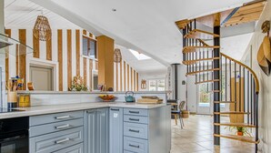 Eine moderne Küche mit einer zentralen Kochinsel, grauen Schränken und einer Holztreppe.
