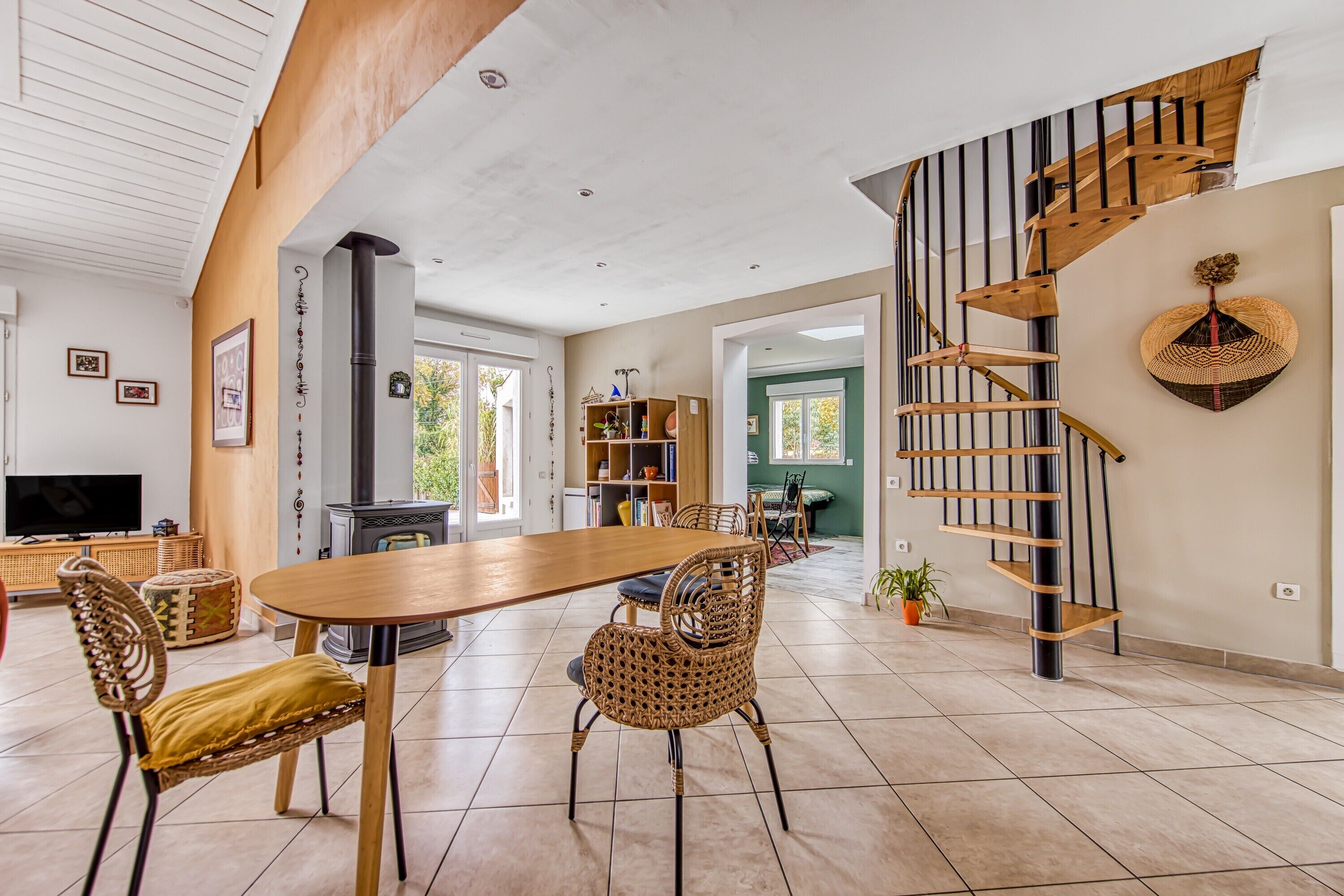 Un vaste espace dédié à la salle à manger, avec une table en bois et des chaises en osier, une cheminée intégrée et un escalier en colimaçon.