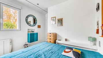 Une chambre à coucher avec un lit, une commode, un miroir et une fenêtre donnant sur des arbres.