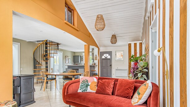 Ein Wohnzimmer mit einem roten Sofa, einem Holztisch und einer Küche im Hintergrund.