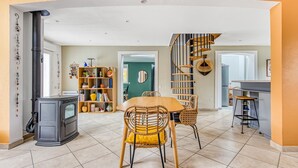 Ein geräumiger Wohnbereich mit Esstisch, Stühlen, Kamin, Bücherregal und Wendeltreppe.