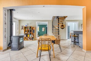 A spacious living area with a dining table, chairs, a fireplace, a bookshelf, and a spiral staircase.