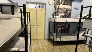 A dormitory room with bunk beds, a wooden floor, a door with a sign, and a wall with a cityscape mural. - TbilHome hostel (Tbilisi)