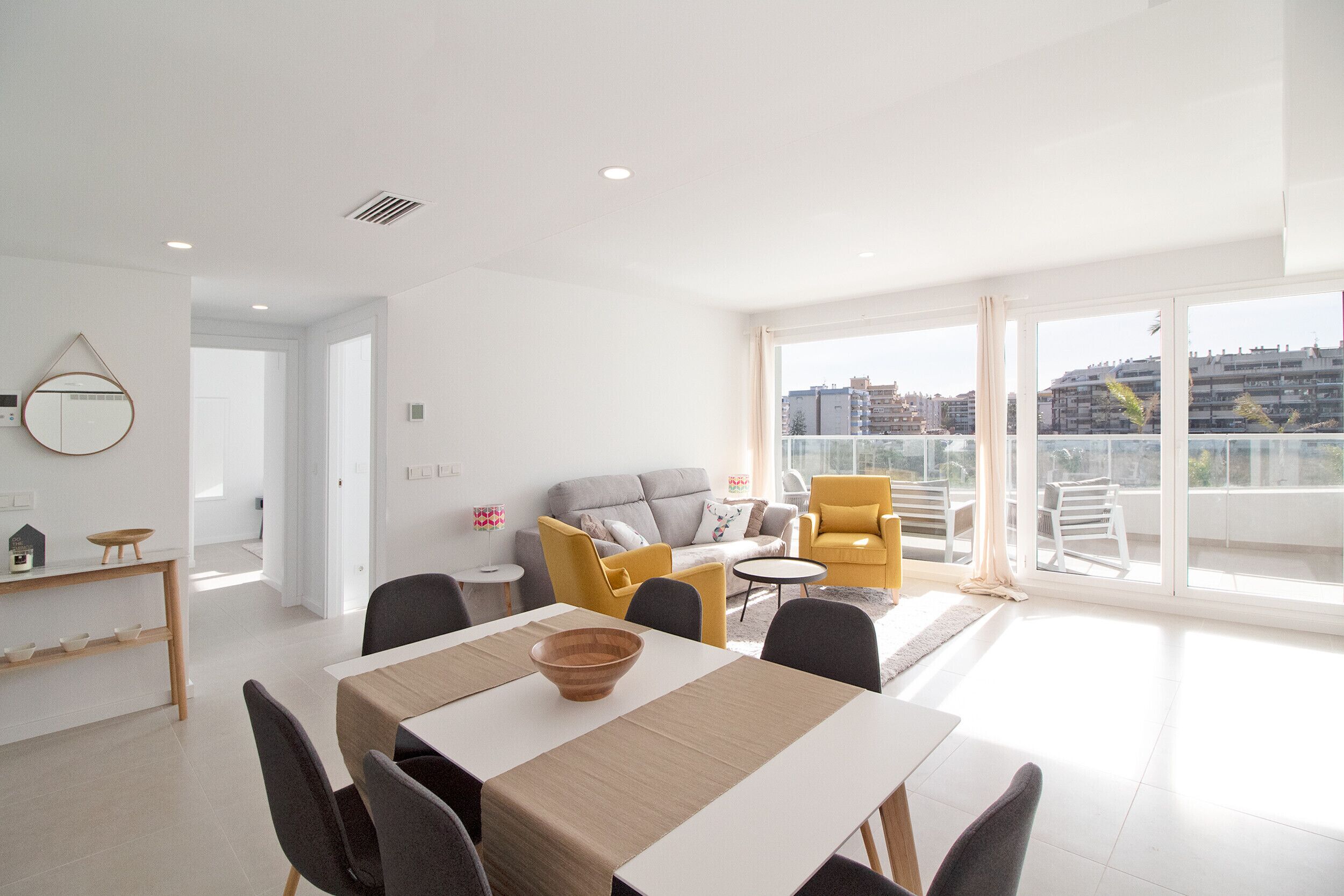 A modern living room with a dining area, a sofa, and a yellow armchair.