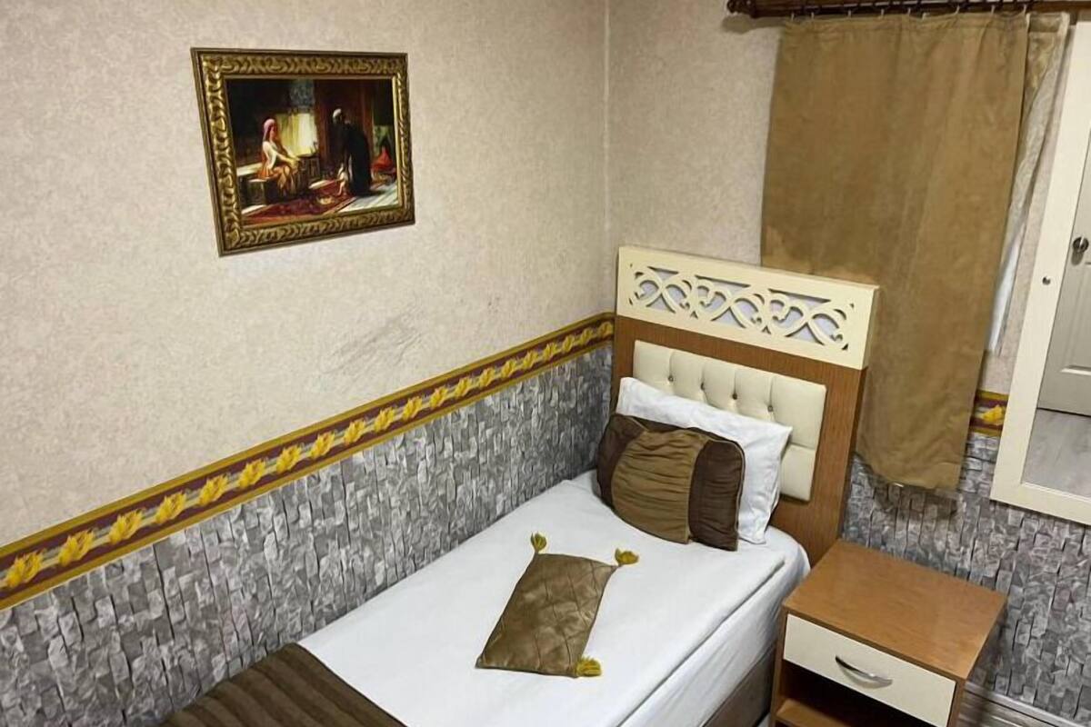 A single bed with a headboard, a bedside table, a nightstand, a framed picture on the wall, and a curtain.