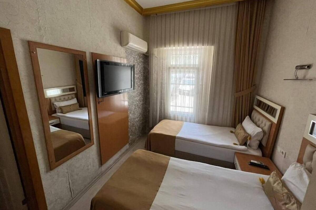 A hotel room with two beds, a television, an air conditioning unit, and a window with curtains.