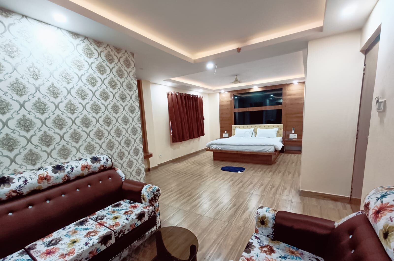 Hotellihuone, jossa on sänky, kaksi sohvaa, pieni pöytä ja kattotuuletin.