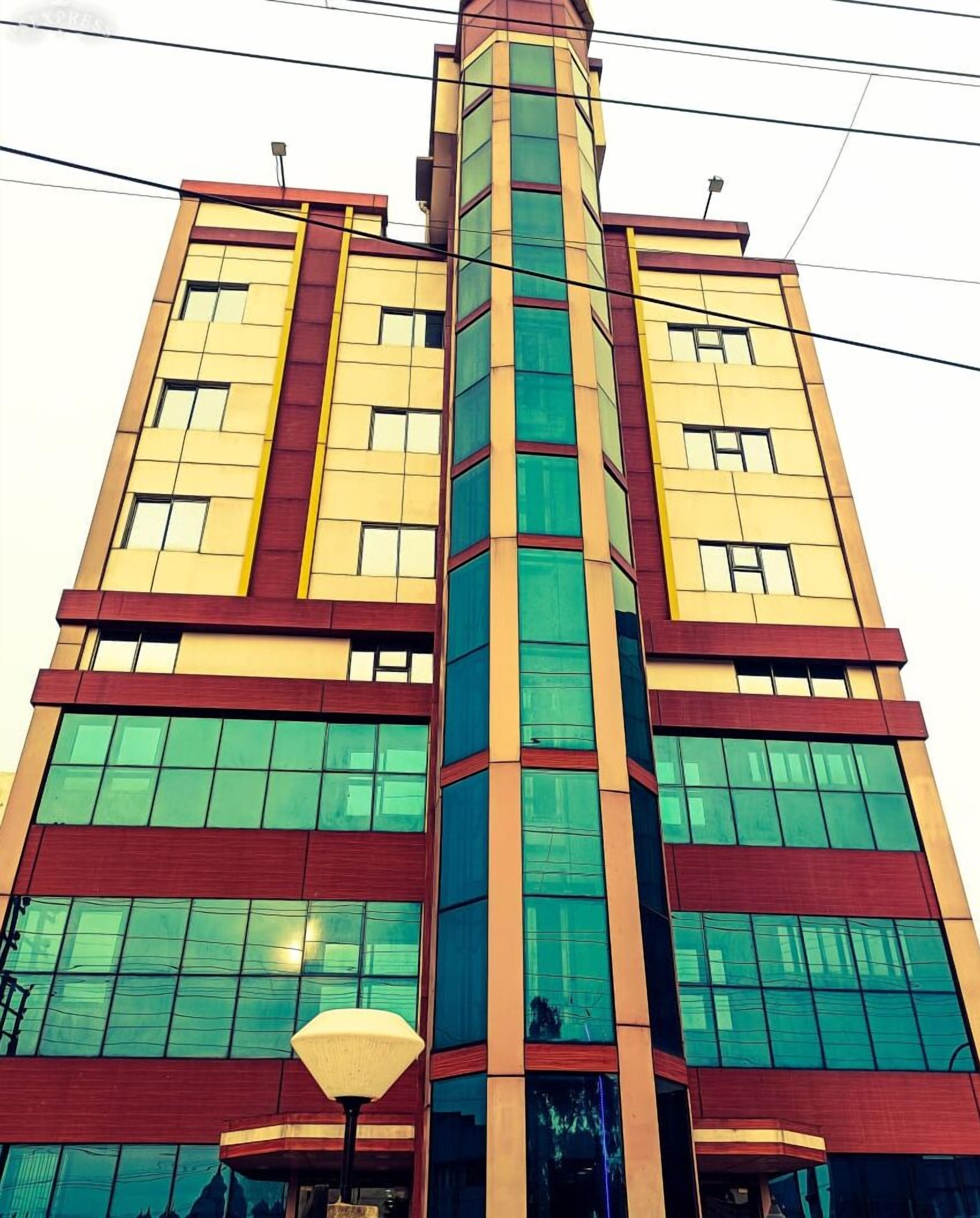 A multi-story building with a central glass tower, large windows, and a red and yellow facade.