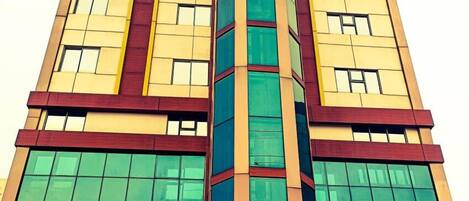 A multi-story building with a central glass tower, large windows, and a red and yellow facade.