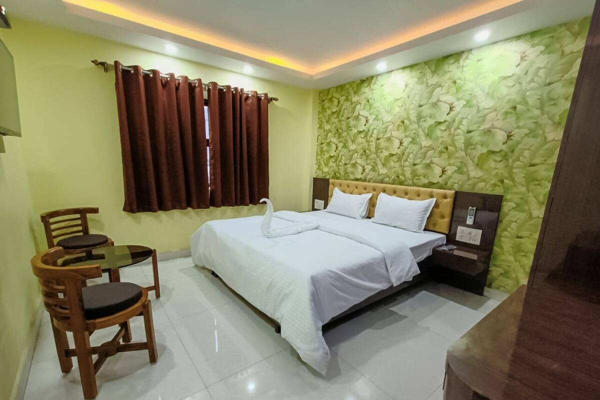 Una habitación de hotel con una cama, una mesita con sillas y una pared con diseño de hojas.