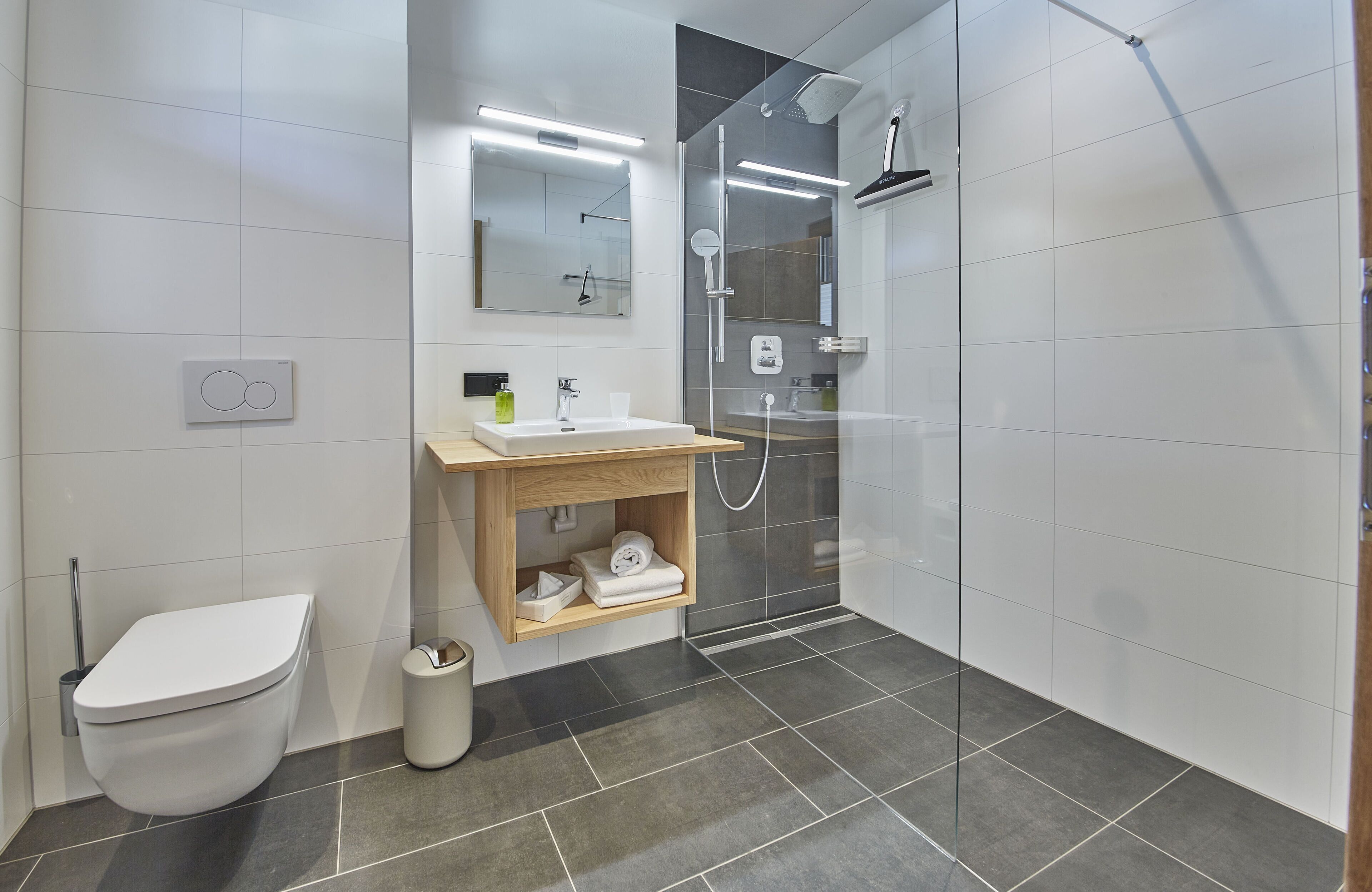 Une salle de bain moderne équipée de toilettes, d’un lavabo, d’un miroir et d’une zone douche.