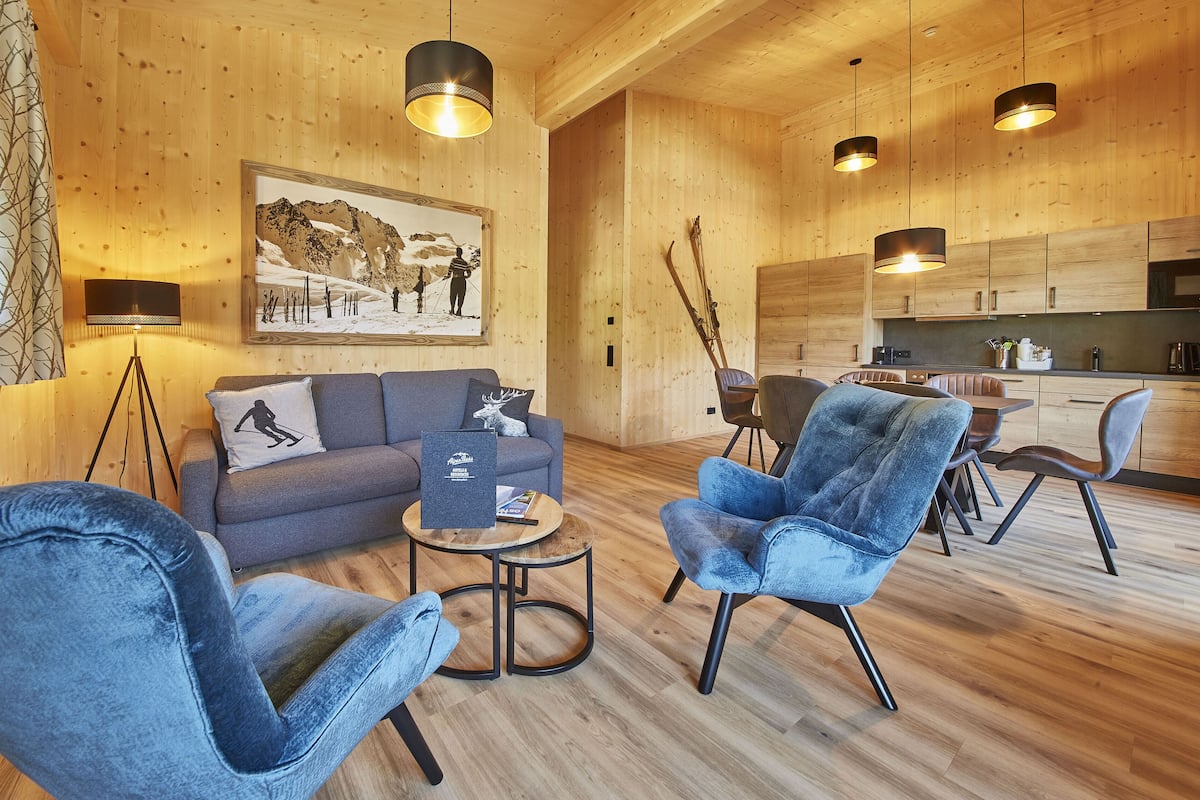 A modern wooden interior with a sofa, two armchairs, a coffee table, and a dining area.