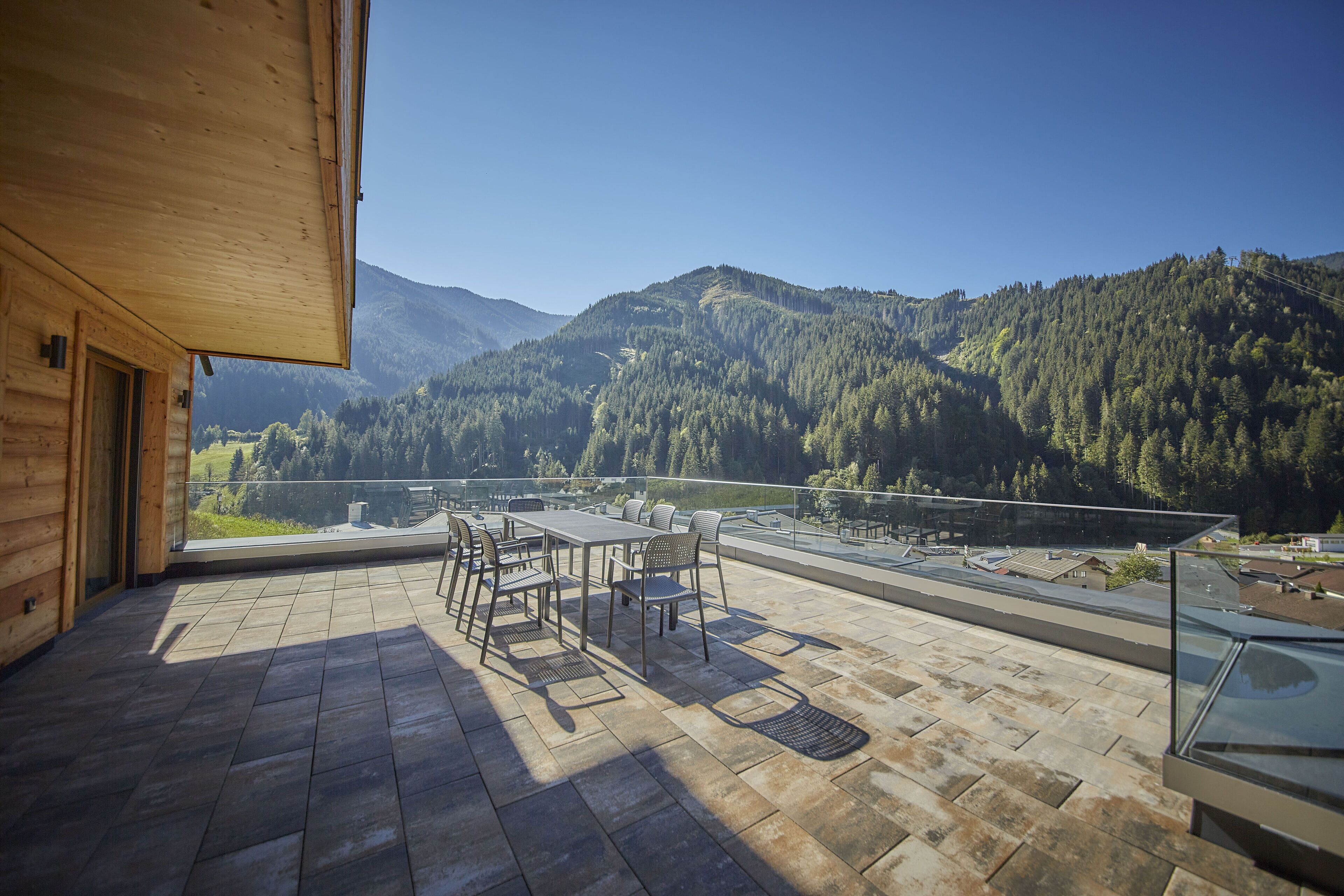 A wooden deck with a table and chairs, overlooking a forested valley and mountains.