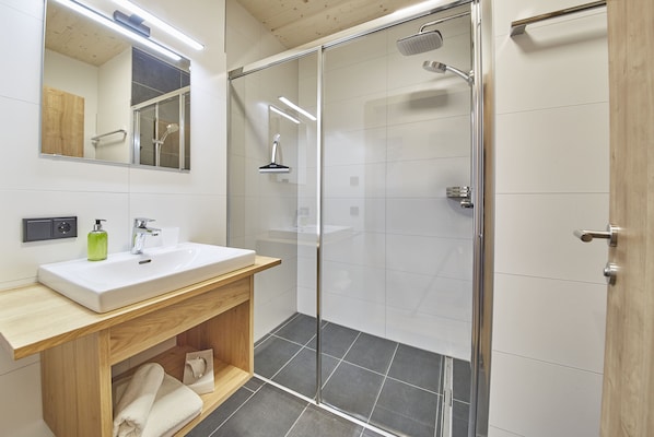 A modern bathroom with a glass shower enclosure, a wooden vanity, and a large mirror.