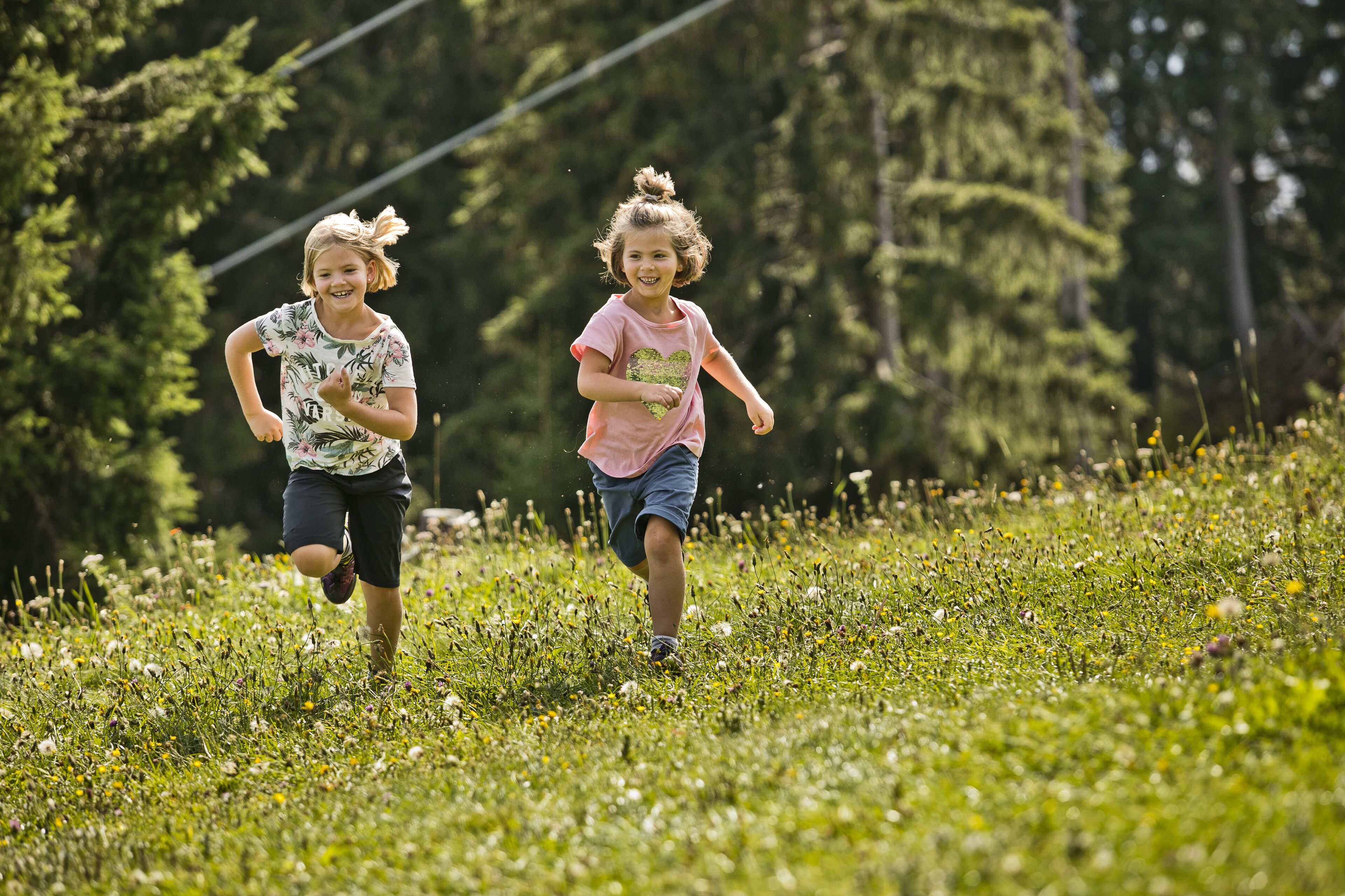 Dos niños corren en un campo de césped con árboles al fondo.