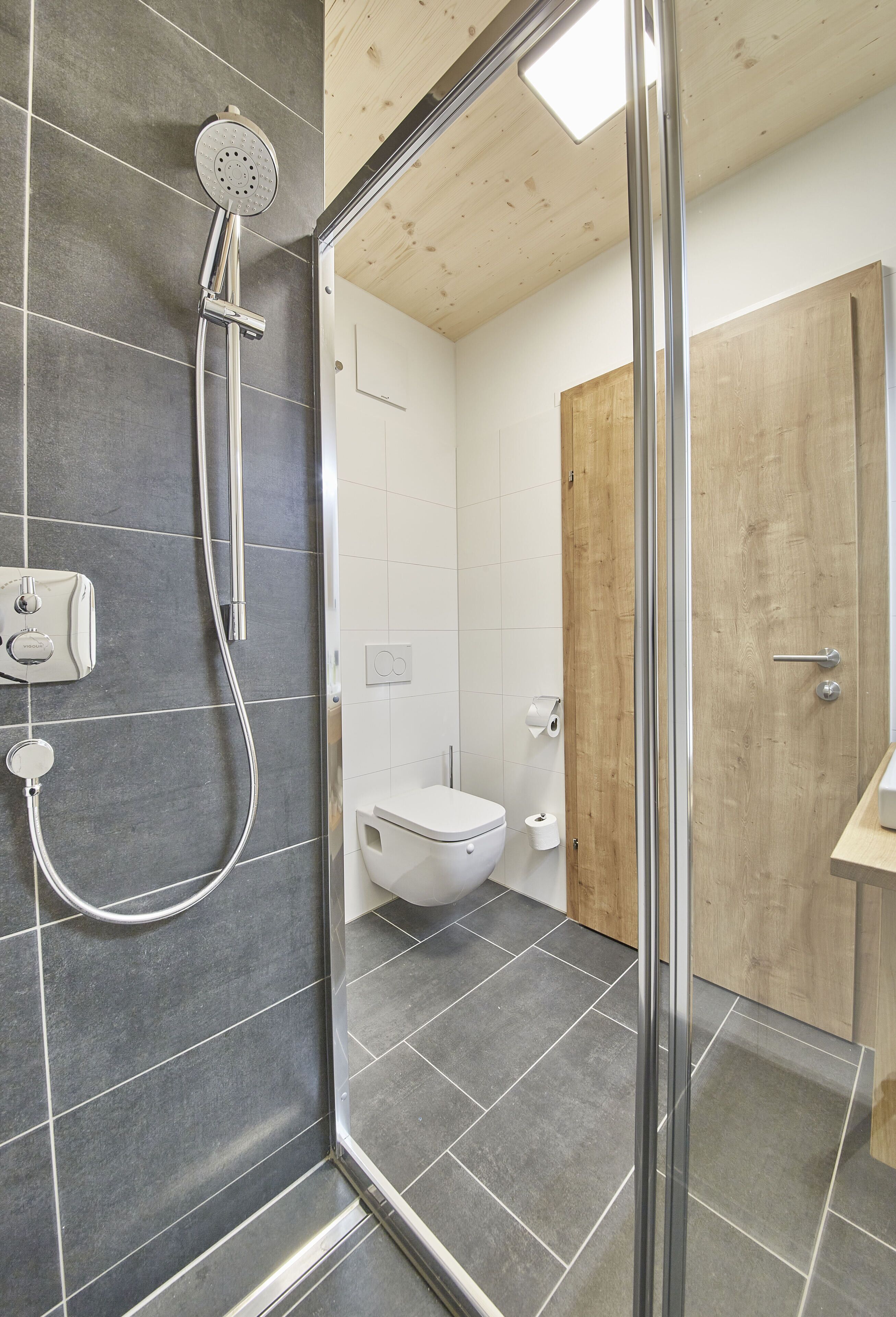 A modern bathroom with a shower, toilet, and wooden door.