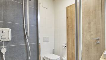 A modern bathroom with a shower, toilet, and wooden door.
