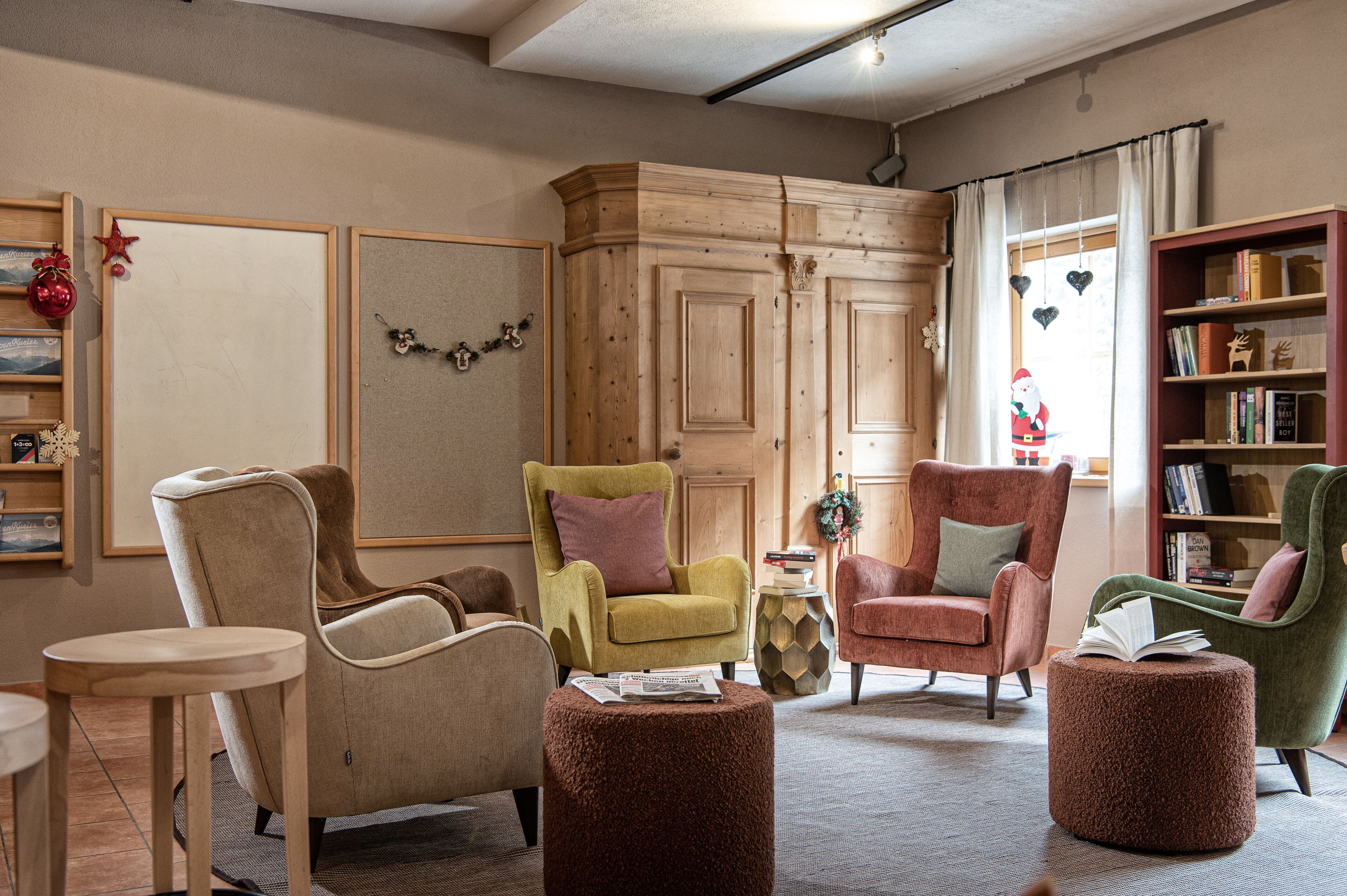 A cozy living room with a wooden cabinet, a green armchair, a red armchair, and a bookshelf.
