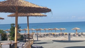 Un patio frente a la playa con sombrillas de paja, sillones de descanso y un comedor.