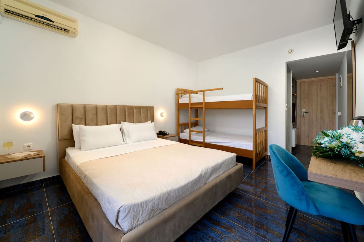 Een slaapkamer met een groot bed, een stapelbed, een bureau met stoel en een nachtkastje met lamp.