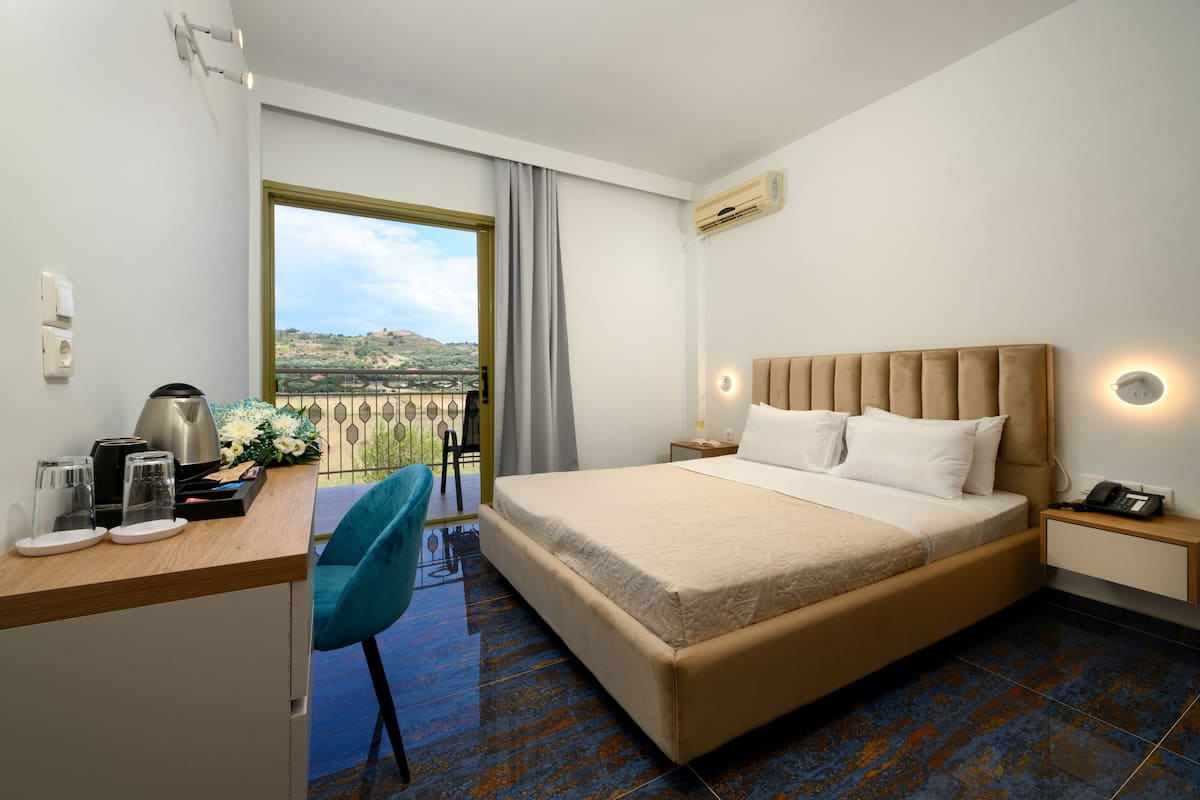 Een hotelkamer met een groot bed, een bureau met stoel, uitzicht op een landschap en een balkon.