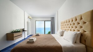 Habitación de hotel con una cama grande, vistas al mar, un pequeño escritorio con una planta y una ventana con cortinas.