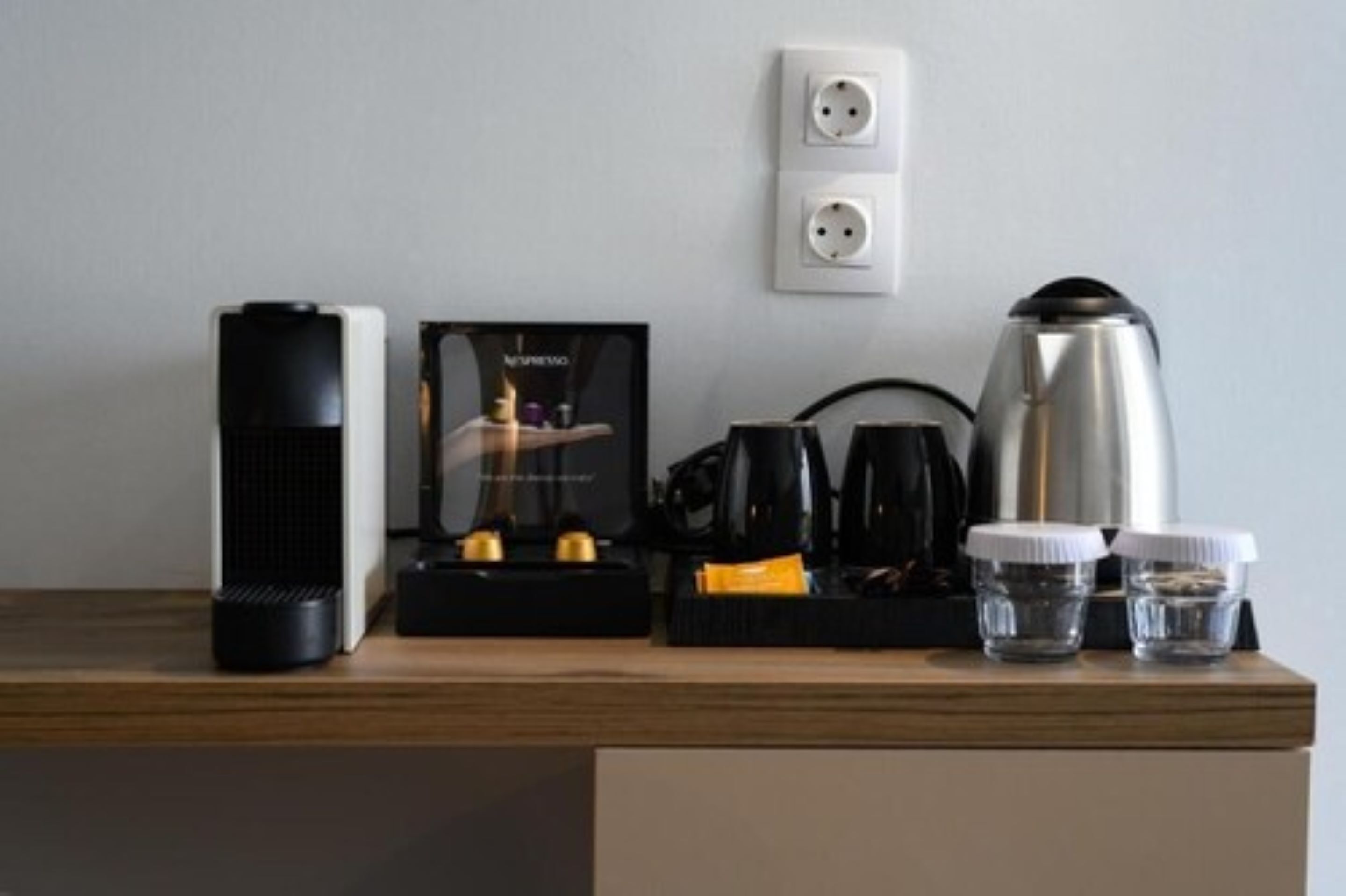 A coffee maker, a kettle, and two cups on a wooden table.