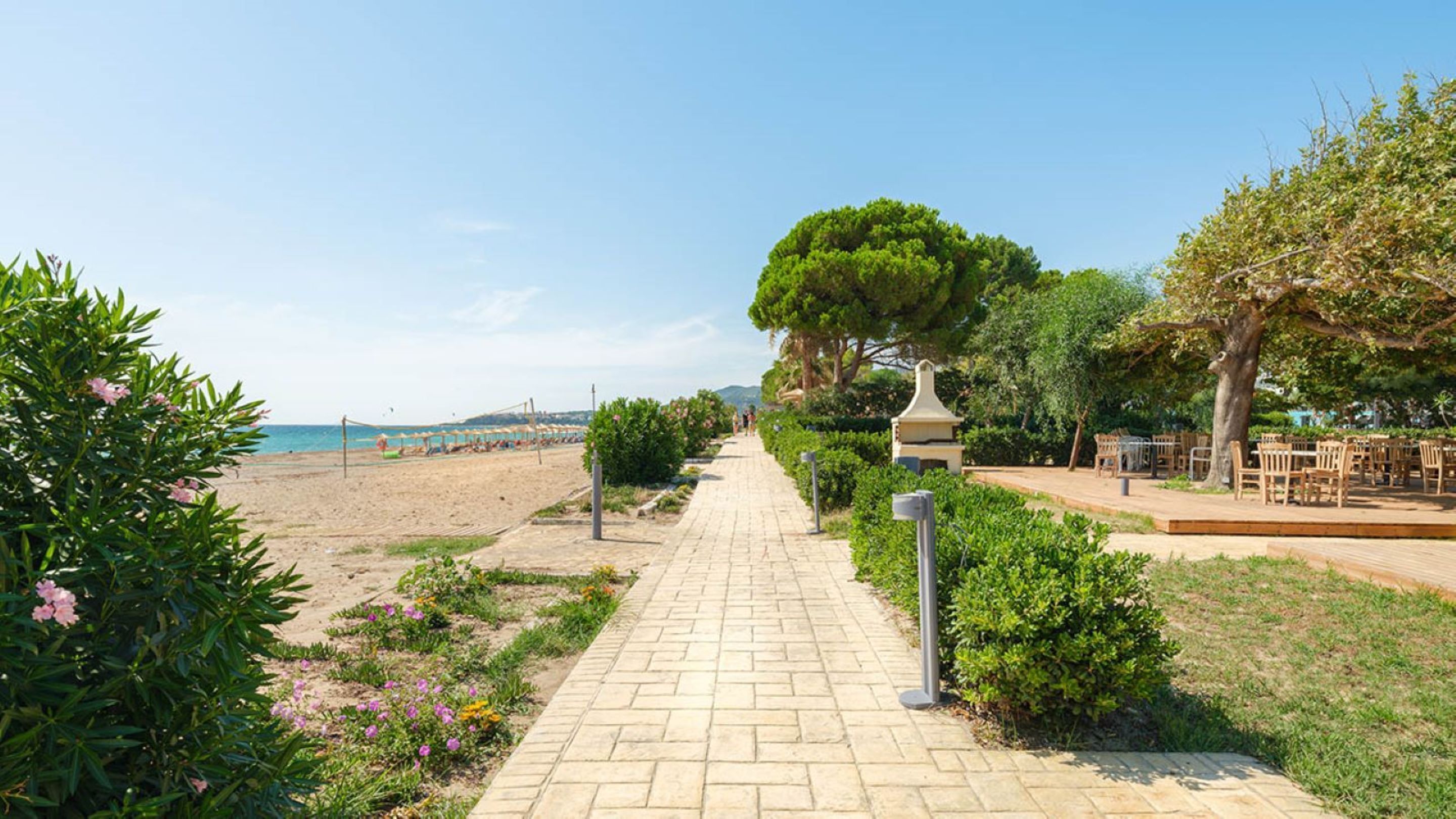 Un camino pavimentado que lleva a una zona de playa con un mirador y mobiliario exterior.