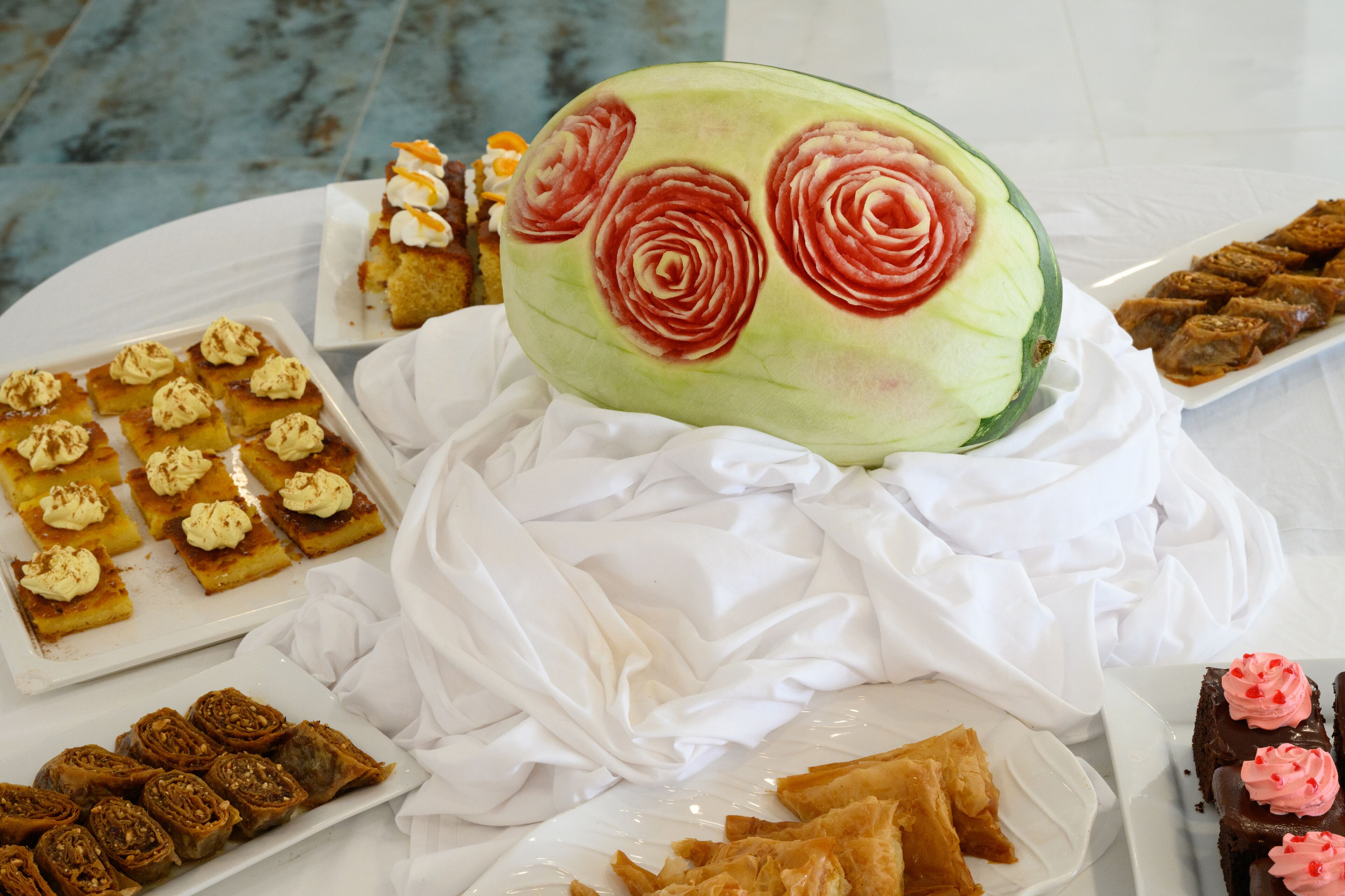 Diverse desserts op een tafel, waaronder een watermeloen uitgehouwen tot een roos.