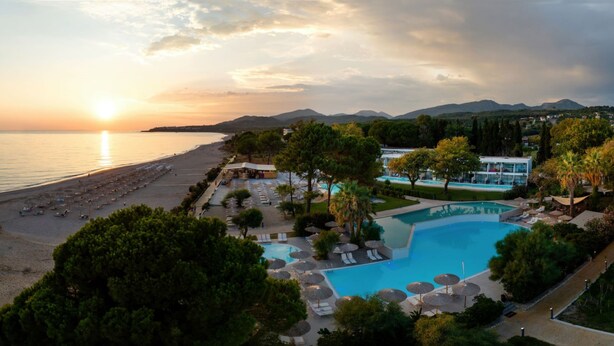 Un resort con playa, piscina y montañas al fondo.