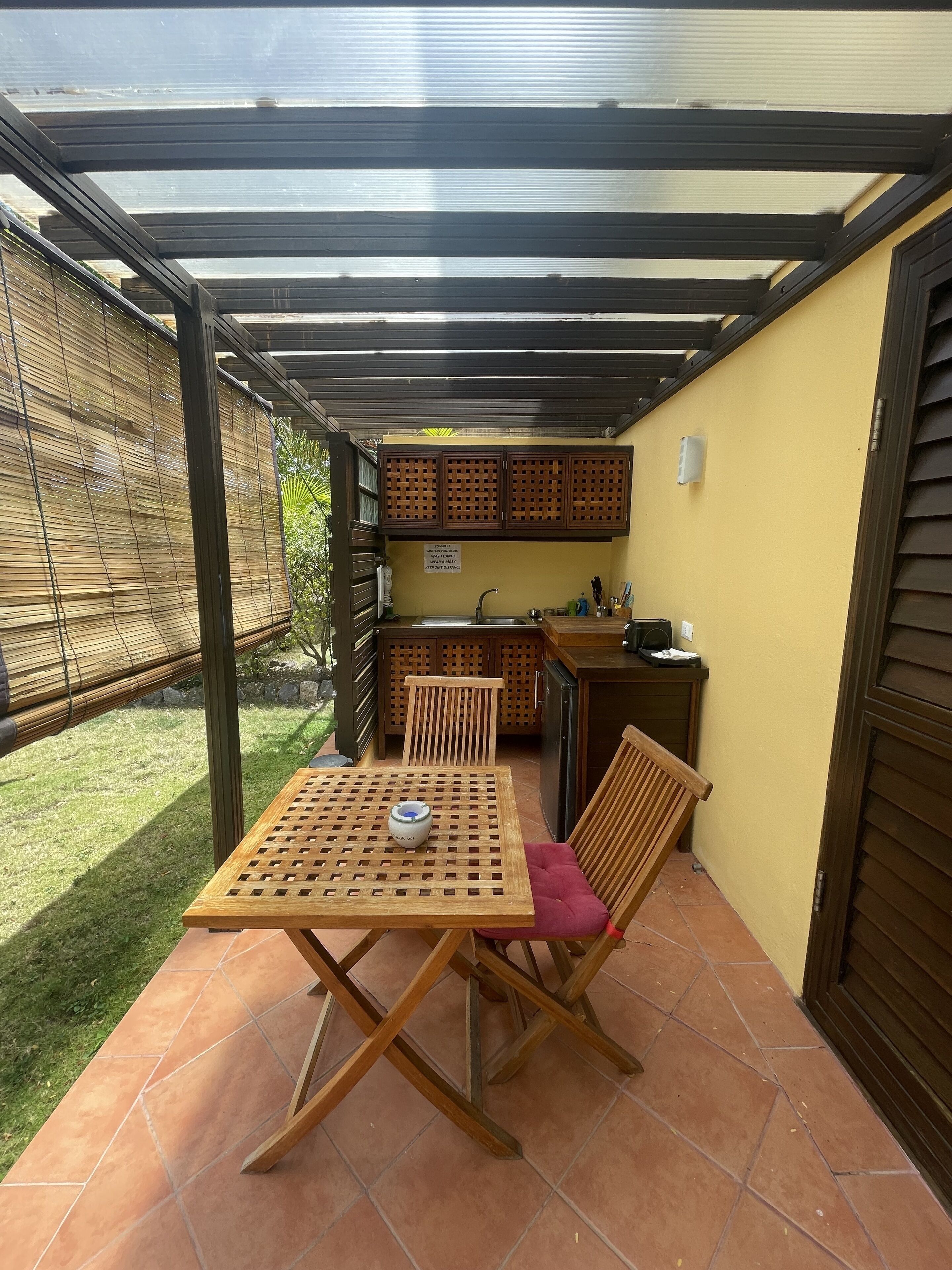 Un patio cubierto con una mesa y sillas, una pequeña cocina y vistas al jardín.