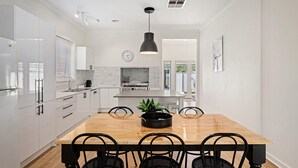 Une cuisine moderne avec des meubles blancs, une table à manger en bois et des chaises noires.