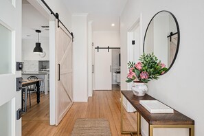 A hallway with a wooden floor, a white door, a mirror, and a vase with flowers. - Frankie's Place - Stunning three bedroom classic in the heart of Wodonga (Wodonga)