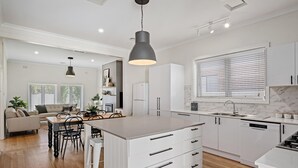 Une cuisine moderne avec des meubles blancs, un îlot central doté de tiroirs, un lave-vaisselle encastré et une grande fenêtre avec des stores.