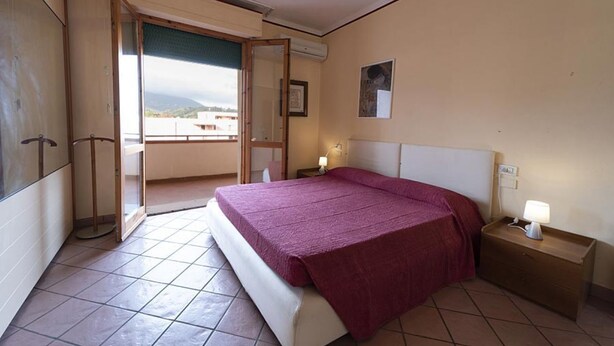 A bedroom with a bed, a nightstand with a lamp, a door leading to a balcony, and a framed picture on the wall.