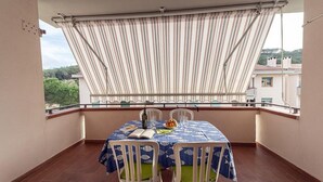 A balcony with a table set for two, a book, a bottle, and a bowl of fruit.