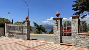 Una entrada protegida con pilares de piedra y portones de metal, que da paso a un camino pavimentado.