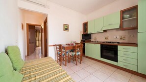 Una cocina compacta con gabinetes verdes, una mesa de comedor con sillas y un sofá en la zona de estar.