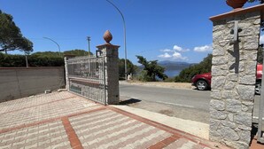 A paved driveway leading to a gated entrance with a stone wall and a red car parked nearby. - Vlletta Grazia 2 apartment (Capoliveri)