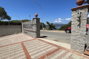 A paved driveway leading to a gated entrance with a stone wall and a red car parked nearby.
