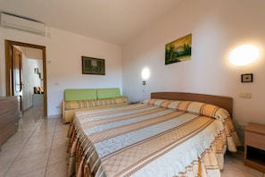 A bedroom with a large bed, a bedside table, a nightstand, a dresser, a green sofa, and a painting on the wall.