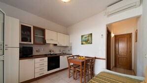 A compact kitchen with white cabinets, a dining table with chairs, a small TV, and a painting on the wall. - Vlletta Grazia 2 apartment (Capoliveri)
