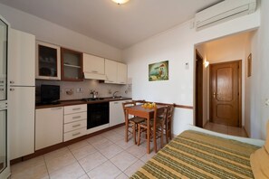 Una cucina compatta con mobili bianchi, un tavolo da pranzo con sedie, una piccola TV e un quadro appeso al muro.