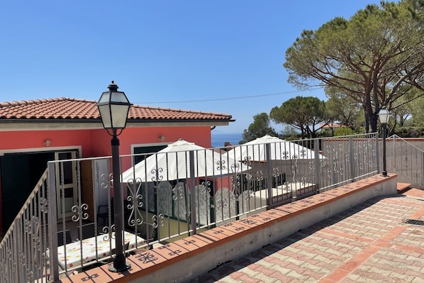 A red building with a tiled roof, a metal fence, and a white umbrella.