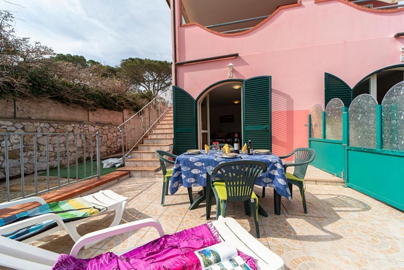 A pink building with a patio area featuring a table with chairs, a pool, and a staircase leading to an upper level.