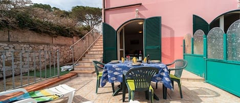 A pink building with a patio area featuring a table with chairs, a pool, and a staircase leading to an upper level.