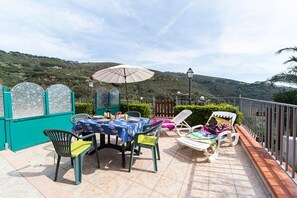 A terrace with a table set for dining, outdoor chairs, and a view of the hills.
