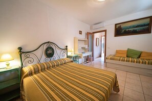 A bedroom with a bed, a desk, a chair, a sofa, and a painting on the wall.