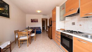 A compact kitchen with wooden cabinets, a gas stove, and a dining area with a table and chairs.