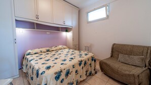 A bedroom with a bed, a sofa, a window, and a cabinet.
